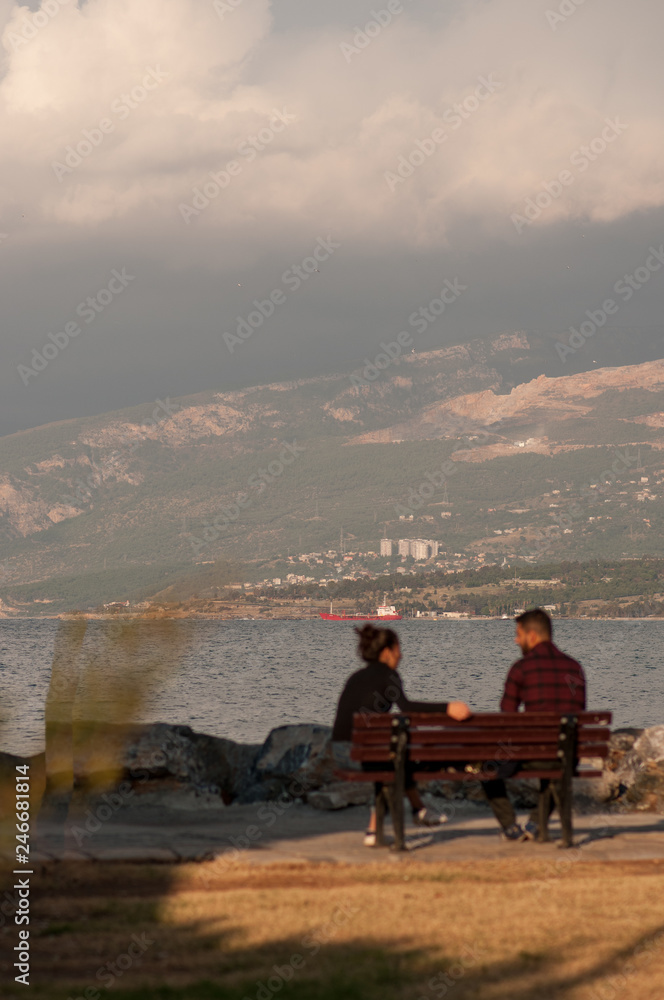Iskenderun, Hatay, Turkey November 16, 2016: a young couple a man and a woman Europeans are having a conversation sitting on a bench at the seashore in autumn on a sunny day