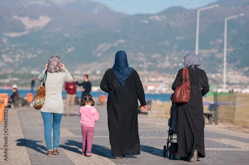 Iskenderun,  Hatay,Turkey November 16, 2016: three Turkish women in national dress and a little girl in pink walking along the embankment in the autumn on a sunny day, view from the back