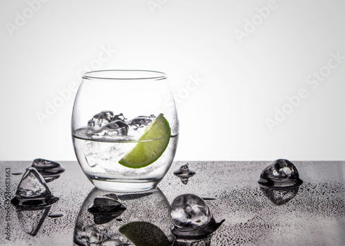 Vodka or Gin with lime in an oval glass on a glossy base with ice cubes against a white back lit background