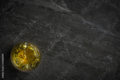 An overhead photograph of a glass of golden Whiskey with ice on a dark marble rock background