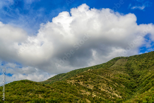 Fluffy white cloud over the green mountain slope