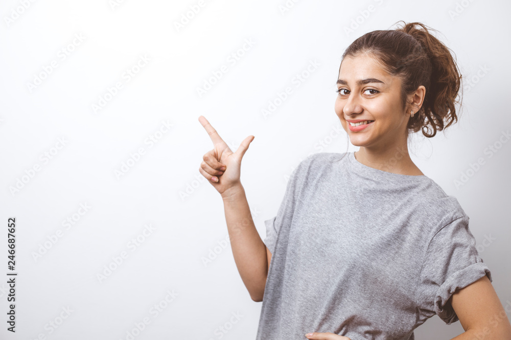 Smiling Indian girl shows fingers on the copy space. Happy young brunette woman points to a blank space on a white background. Smiling Indian girl shows fingers on the copy space. Happy young brunette woman points to a blank space on a white background.