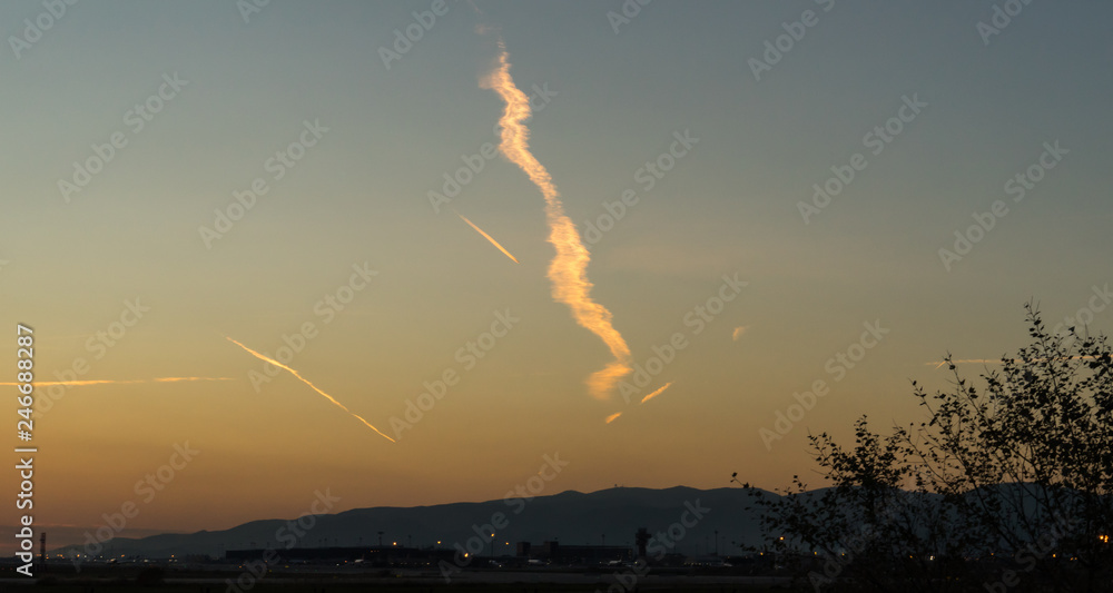 sky with some clouds making by planes in the sunset time and a mountain