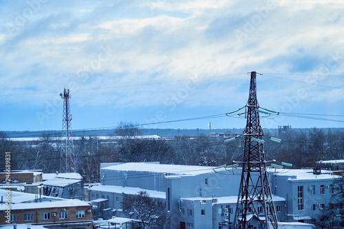 Power transmission line tower against blue sky and clouds with snow-covered high-voltage insulators