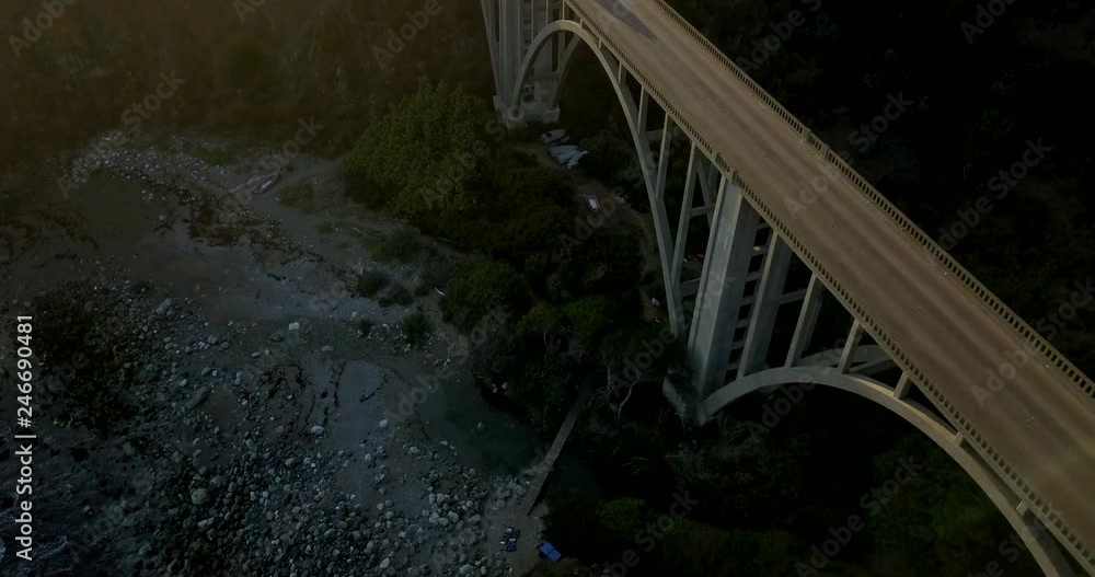 Silver SUV crosses costal bridge spanning mountains at sunset - aerial shot tilting down Silver SUV crosses costal bridge spanning mountains at sunset - aerial shot tilting down