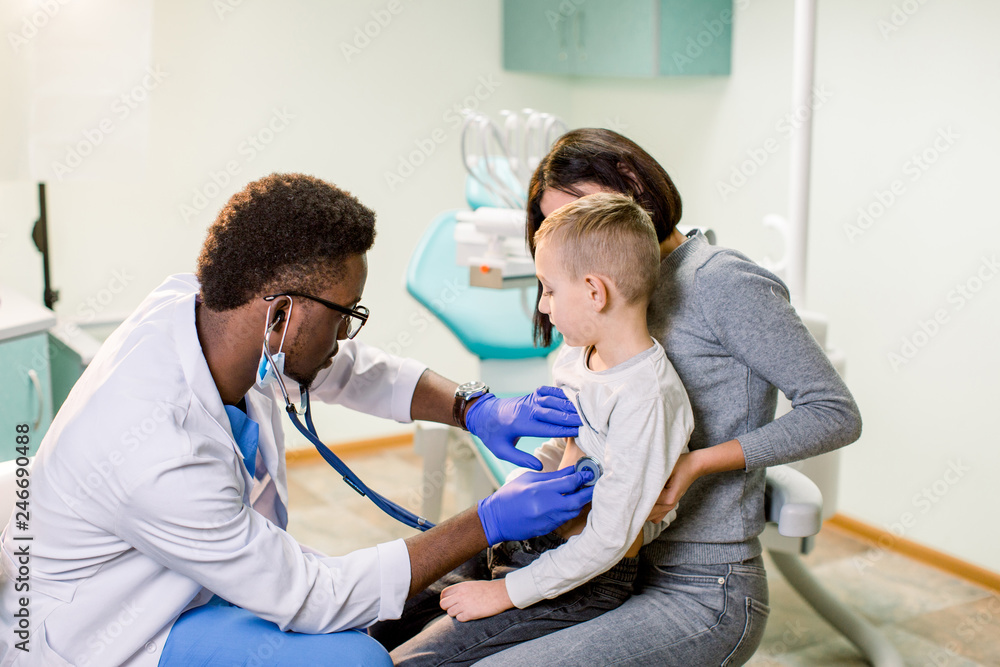 medicine, healthcare, pediatry and people concept - happy woman with her son and African American doctor with stethoscope at clinic medicine, healthcare, pediatry and people concept - happy woman with her son and African American doctor with stethoscope at clinic
