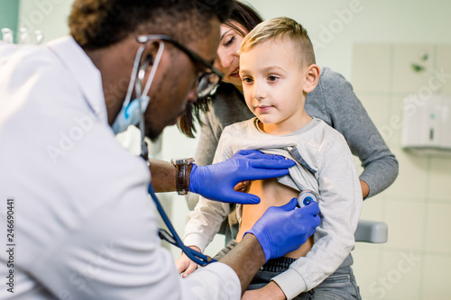 medicine, healthcare, pediatry and people concept - happy woman with her son and African American doctor with stethoscope at clinic