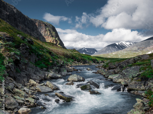 Long exposure of a river with stones in front of mountains while walking Kungsleden  Kings path  hike in northern Sweden during summer. 