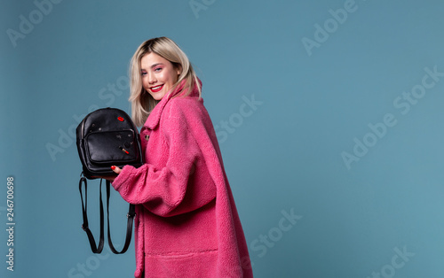 Beautiful blonde girl wearing pink coat holding black backpack in hands