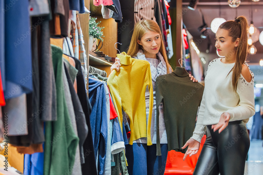 Two friends choose sweaters during shopping. Feel good, smiling and laughing. Two friends choose sweaters during shopping. Feel good, smiling and laughing.