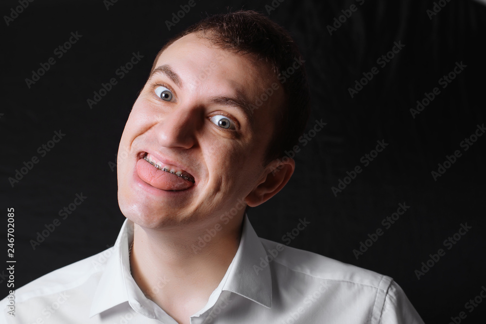 Portrait of a man of Caucasian appearance in orthodontic braces, metal brackets on his teeth in a white shirt on a black background. Dental concept, medicinal alignment of teeth orthodontist. Portrait of a man of Caucasian appearance in orthodontic braces, metal brackets on his teeth in a white shirt on a black background. Dental concept, medicinal alignment of teeth orthodontist.