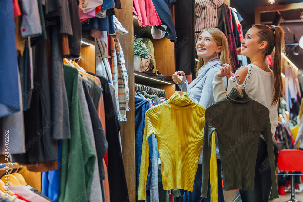 Two friends choose sweaters during shopping. Feel good, smiling and laughing.