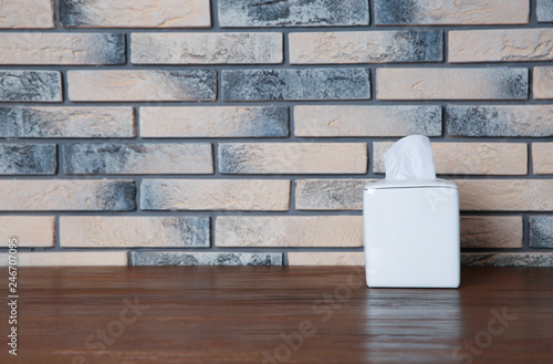 Napkin holder with paper serviettes on table against brick wall. Space for text
