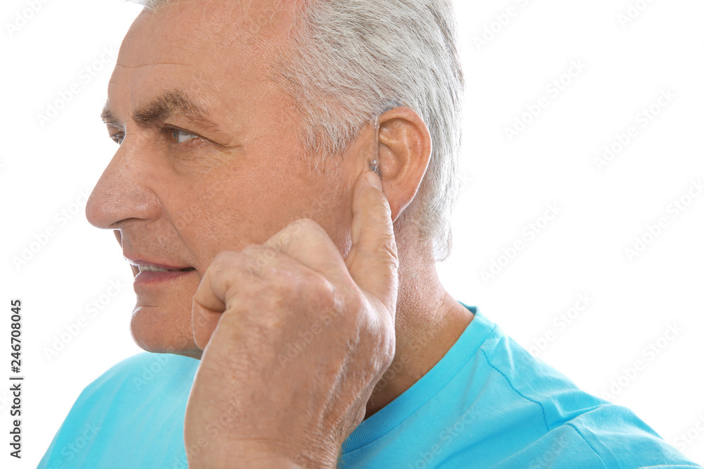 Obraz premium Mature man adjusting hearing aid on white background
