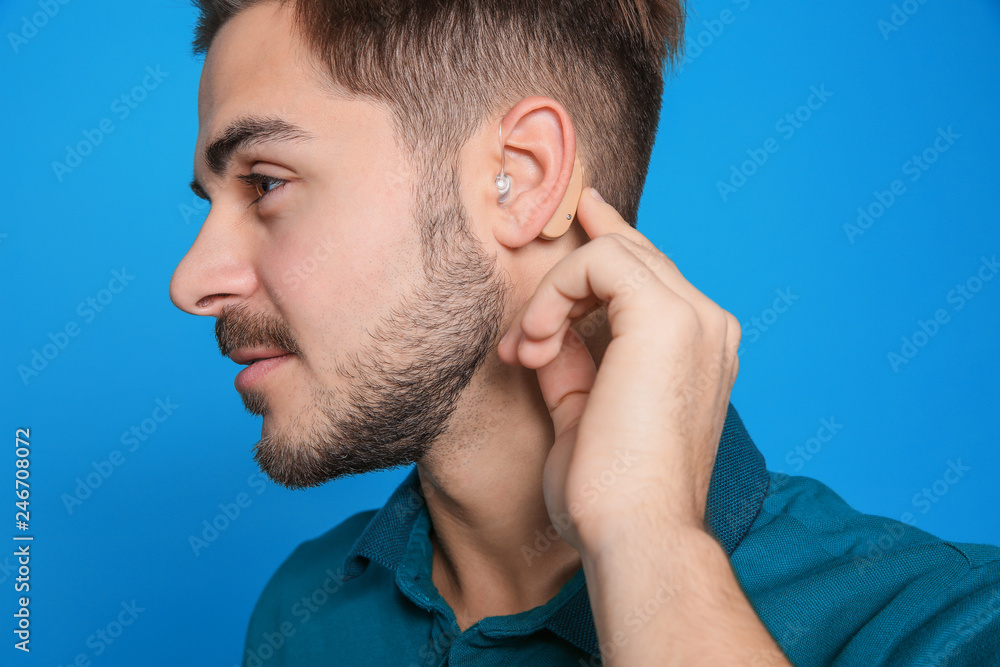 Young man adjusting hearing aid on color background Young man adjusting hearing aid on color background