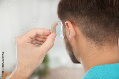 Fototapeta Naklejka Na Ścianę i Meble -  Young man putting hearing aid in ear indoors, closeup