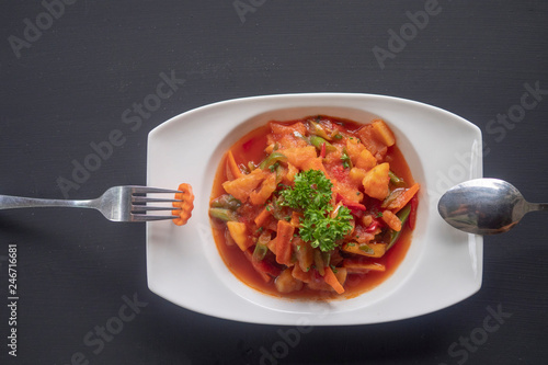 vegetable stew of potatoes, paprika, tomatoes and carrots on a white plate on a dark background photo