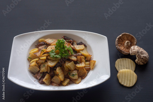 fried potatoes with mushrooms on a white plate on a dark background