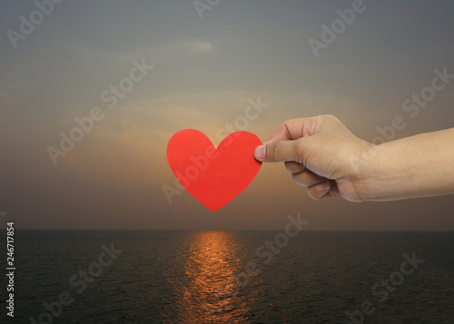 Woman s hand holding a red heart on sunset background in concept of love and Valentine s Day.