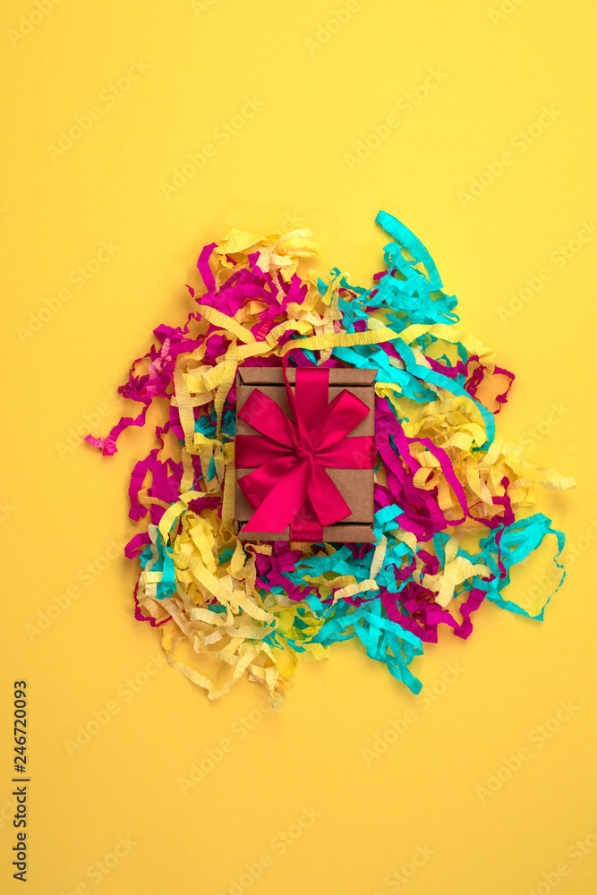 Gift box with colored streamers bright yellow background top view of Flat lay