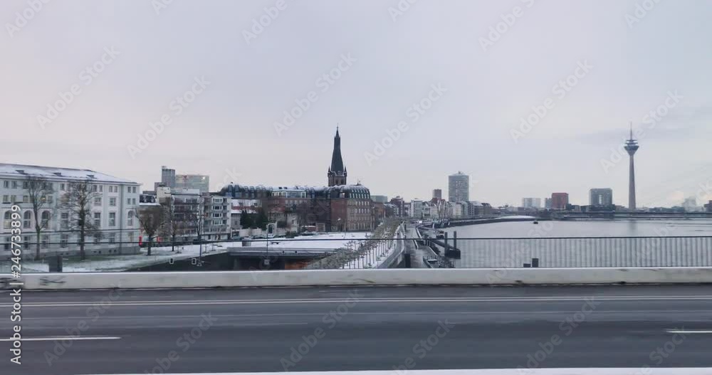 Panoramic view of snow cover promenade riverside and old town city skyline of Düsseldorf city from moving train on the bridge cross Rhine river and background of overcast sky in winter season.