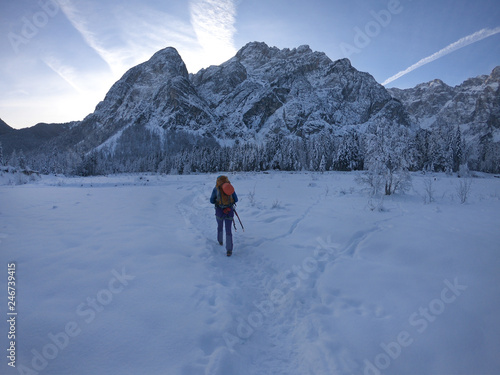 Young sports woman backpacker tourist walkingin winter landscape in the early morning. Saisera valley, Julian Alps, Italy photo