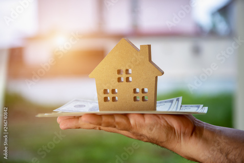 hand a businessman Investing and saving money or borrowing money from financial institutions to buy home for the future is a valuable asset in the concept of house model coupled with dollar banknotes.