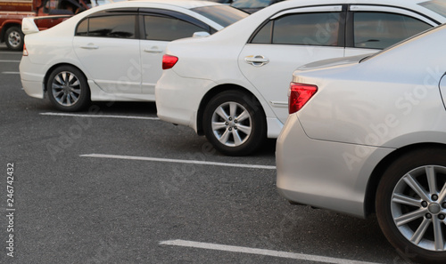 Closeup of back or rear side of silver car and white cars parking in parking area in the evening of sunny day. 