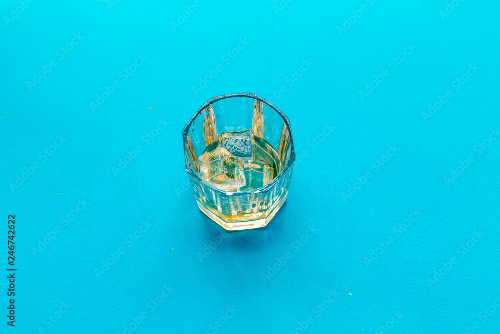 Glass of whiskey with ice on blue background top view copy space Glass of whiskey with ice on blue background top view copy space
