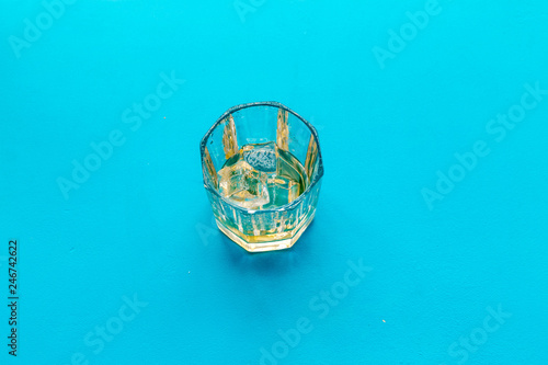 Glass of whiskey with ice on blue background top view copy space