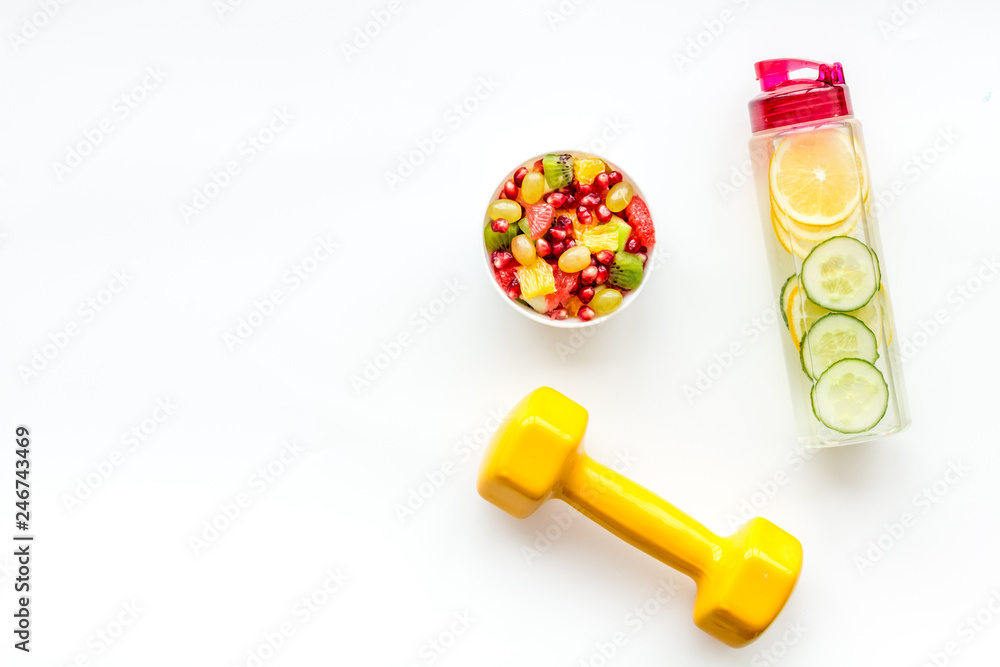 Healthy lifestyle, healthy habits. Detox water, fruit salad, sport equipment dumbbells on white background top view copy space Healthy lifestyle, healthy habits. Detox water, fruit salad, sport equipment dumbbells on white background top view copy space
