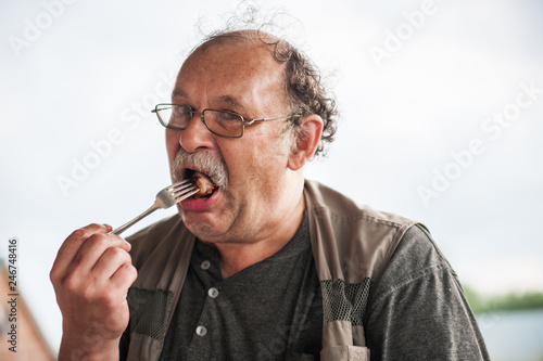 Adult man with glasses and a mustache puts in his mouth a piece of meat