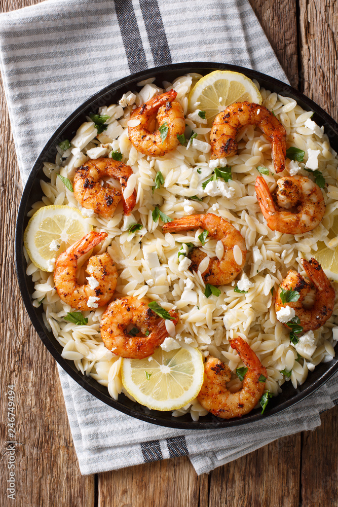 Orzo pasta with grilled shrimps, feta cheese and lemon close-up on a plate. Vertical top view Orzo pasta with grilled shrimps, feta cheese and lemon close-up on a plate. Vertical top view