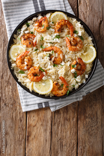Mediterranean food Pasta orzo with grilled shrimps, feta cheese and lemon close-up on a plate. Vertical top view