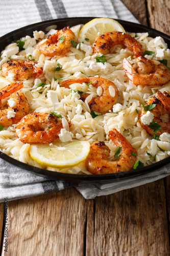 Italian pasta orzo with grilled shrimps, feta cheese and lemon closeup on a plate. vertical