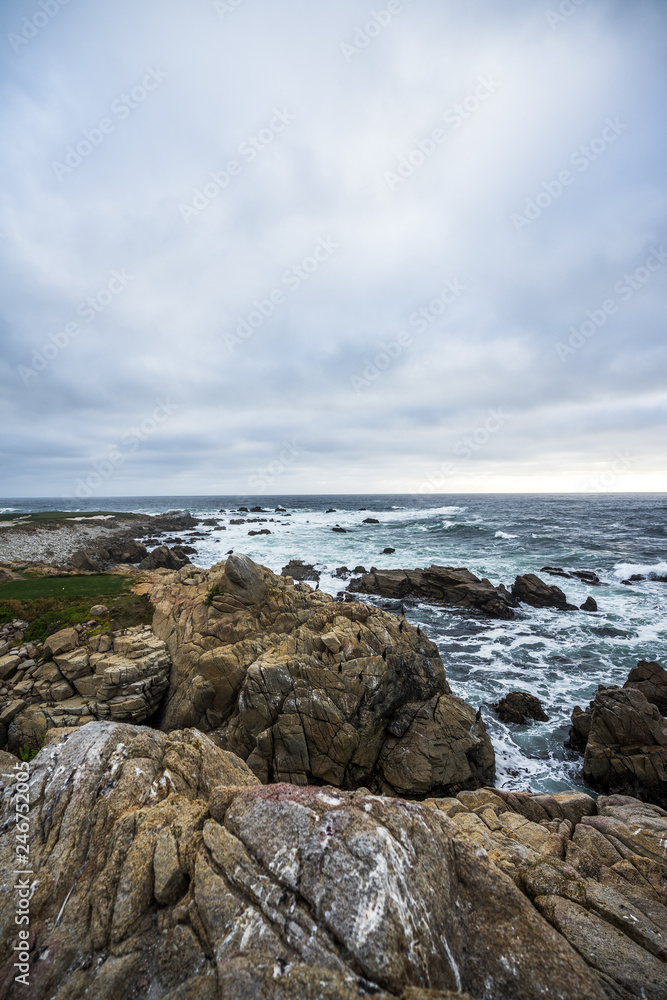 Ocean waves crashing on rocks, coastline view in California. Sand and rocks on a beach