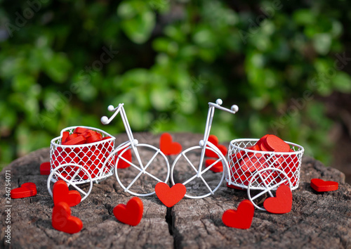 White toy bike carrying red wooden hearts. Red wood hearts fall on the wooden floor. Heart-shaped toys convey to Valentine's Day.
