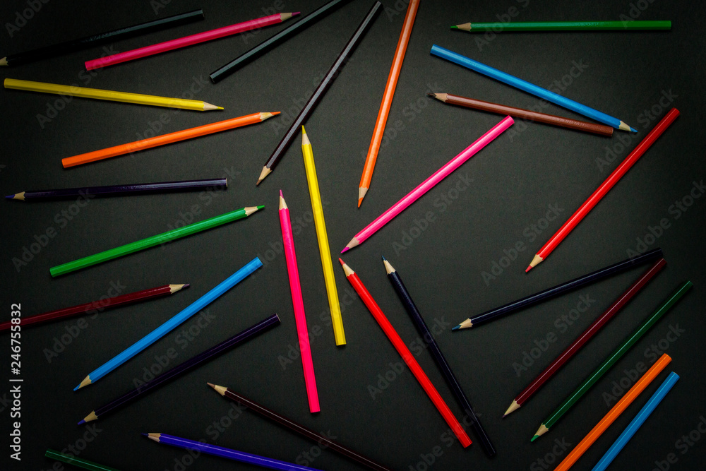 Color pencils scattered throughout the frame on a black background. Flat lay, top view Color pencils scattered throughout the frame on a black background. Flat lay, top view