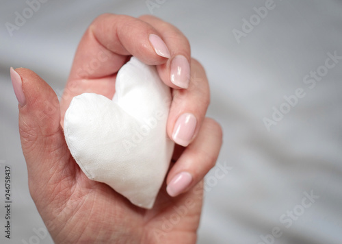 white handmade fabric heart in woman s hand in grey background - image