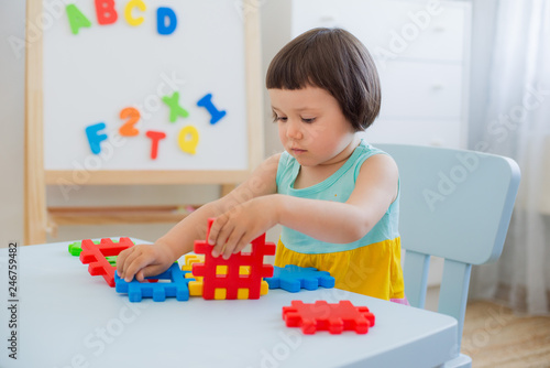 A 3 year old child plays at a table with colorful toy blocks. Children play with educational toys in the kindergarten or room. Preschoolers gather at the table the puzzle out of plastic blocks.