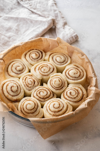 Raw cinnamon rolls in baking plate on kitchen table. Copy space.