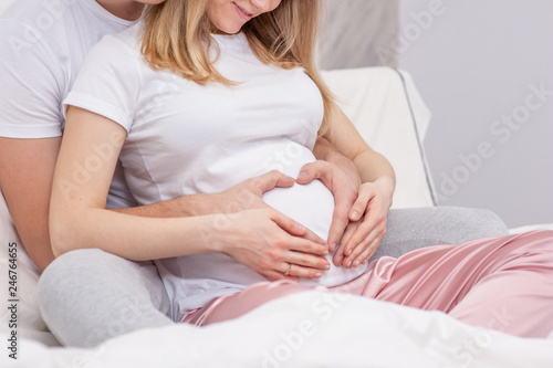 Happy young family. Pregnant woman and her husband hugging on the bed