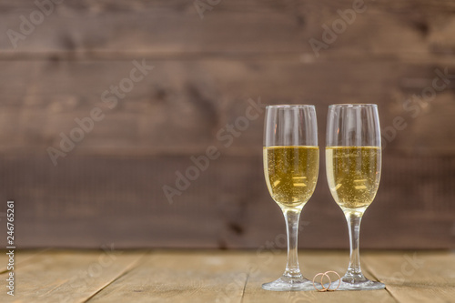 Pair glass of champagne with golden wedding rings on wooden background. Empty space for your text