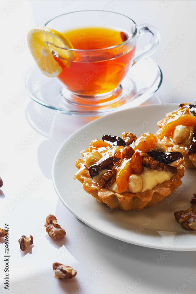 Basket-cake with nuts, dried fruits and jelly on white plate. Cup of tea. Closeup. Selective focus. Basket-cake with nuts, dried fruits and jelly on white plate. Cup of tea. Closeup. Selective focus.
