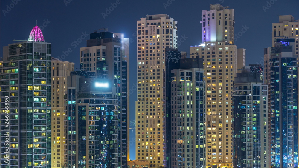 Glowing windows in multistory modern glass and metal residential buildings light up at night timelapse.
