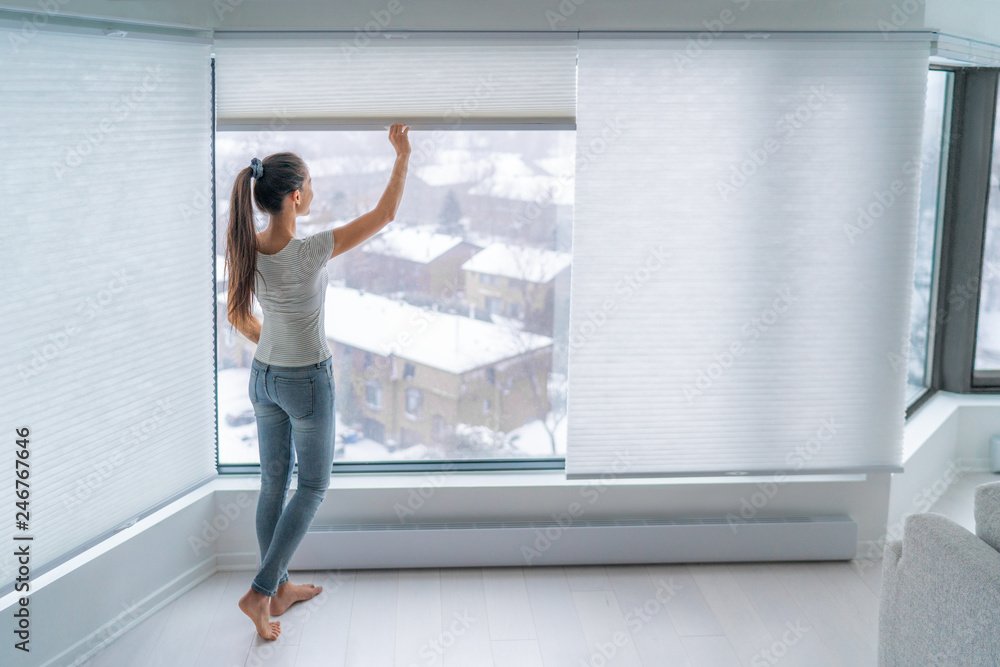 Fototapeta Kobieta zamykająca komórkowe żaluzje w oknie mieszkania, utrzymująca energię i ciepło w pomieszczeniu za pomocą zasłony o strukturze plastra miodu. Bezprzewodowe plisy w nowoczesnym stylu życia w domu. Projektowanie wnętrz