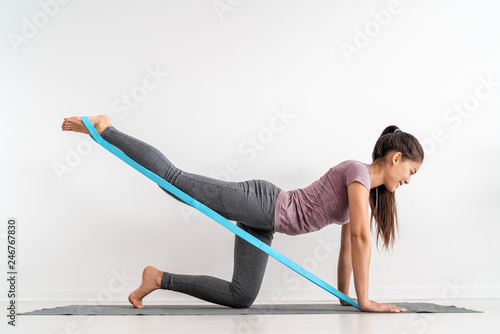Resistance band fitness girl doing leg workout donkey kick floor exercises with rubber strap elastic. Glute muscle activation with kickback for cellulite.