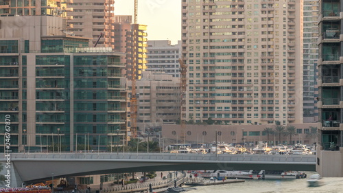 Yachts and boats with tourists staying near shoping mall and passing under a bridge in Dubai Marina district timelapse.