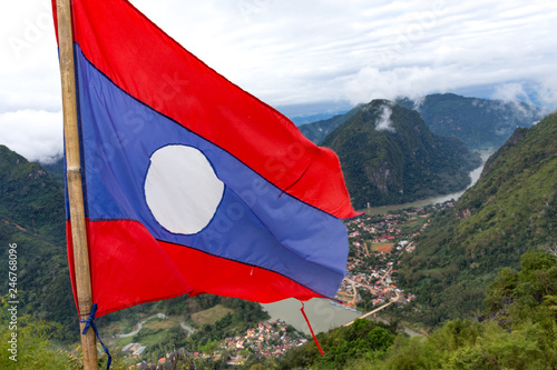 Laos flag on top of Viewpoint of Nong Khiaw - a secret village in Laos. Stunning scenery of limestone cliff valley covered with green rainforest jungle mysterious clouds. A gem of north Laos. photo