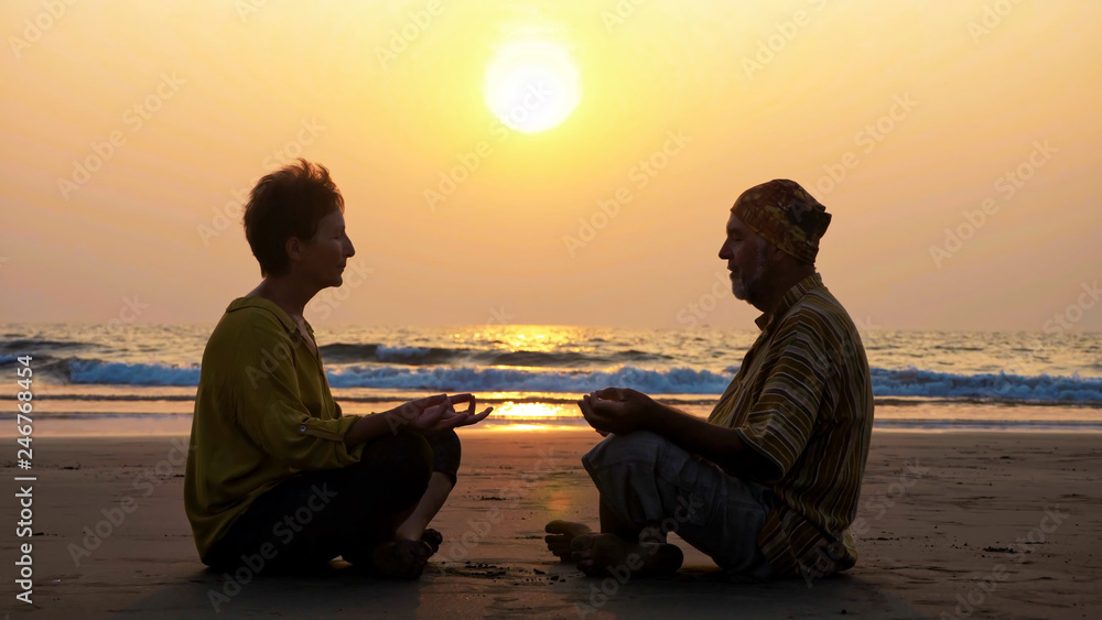 Silhouette of senior couple sits and meditating together on sandy beach